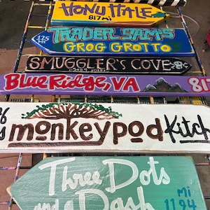 K&ouml;nnte beinhalten: Eine Sammlung handbemalter Holzwegweiser. Ziele sind Washington DC, Pensacola Beach, Honu Itale, Trader Sam's Grog Grotto, Smuggler's Cove, Blue Ridge VA, Monkeypod Kitchen und Three Dots and a Dash.