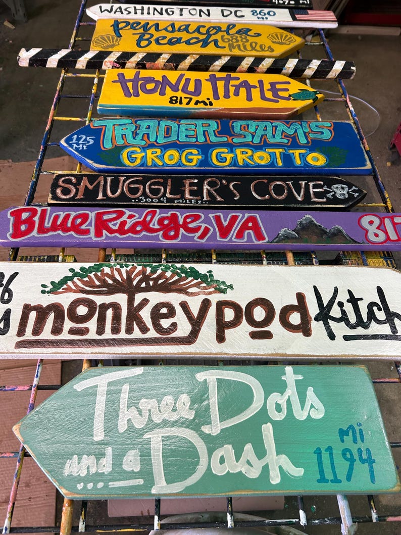 K&ouml;nnte beinhalten: Eine Sammlung handbemalter Holzwegweiser. Ziele sind Washington DC, Pensacola Beach, Honu Itale, Trader Sam's Grog Grotto, Smuggler's Cove, Blue Ridge VA, Monkeypod Kitchen und Three Dots and a Dash.