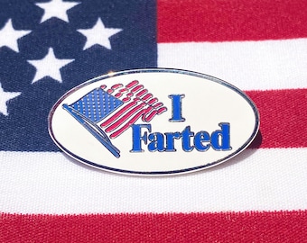 May include: A white oval-shaped button with a red, white, and blue American flag design and the text "I Farted" in blue letters.