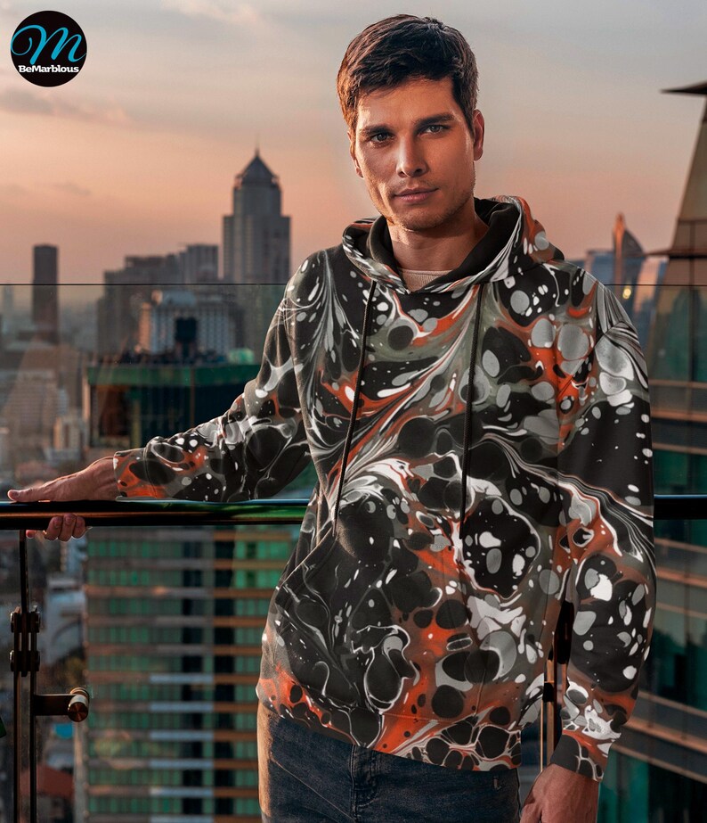 May include: A black hoodie with a swirling abstract pattern in shades of orange, white, and gray. The hoodie has a drawstring hood and a kangaroo pocket.