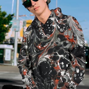May include: A black hoodie with a red, white, and gray marbled pattern. The hoodie has a drawstring hood and a kangaroo pocket.