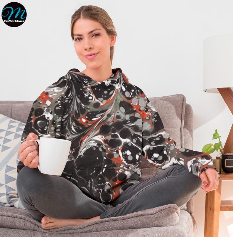 May include: A black, white, and orange marbled hoodie with a drawstring hood. The hoodie has a large pocket on the front.