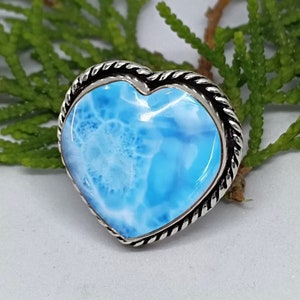 May include: A heart-shaped ring with a blue and white Larimar gemstone set in a silver band with a rope-like design.