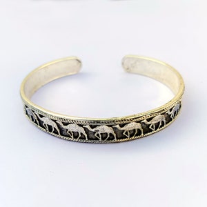 May include: A silver bracelet with a design of camels walking in a line around the band.