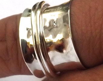 May include: A silver ring with a hammered texture and a smooth, polished band. The ring has a wide band with a textured surface and a smaller, smooth band that wraps around it. The ring is worn on a finger.