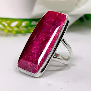 May include: A silver ring featuring a large, rectangular, pink ruby gemstone. The ruby has a deep, rich colour and is set in a simple, elegant band.