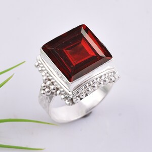 May include: A silver ring with a large, square, red gemstone. The ring has a detailed, textured band.