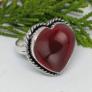 May include: A silver ring with a red heart-shaped gemstone. The ring has a rope-like design around the edge of the setting.