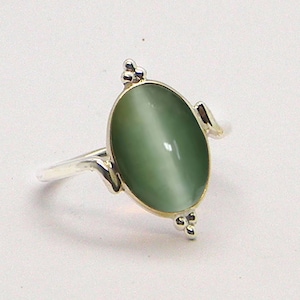 May include: A silver ring with a green oval-shaped gemstone. The ring has a delicate design with small beads on either side of the stone.