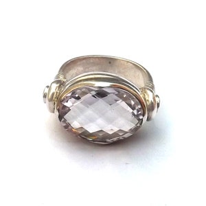 May include: A silver ring featuring a large, faceted, oval-shaped amethyst gemstone. The ring has a twisted band and a gold accent.