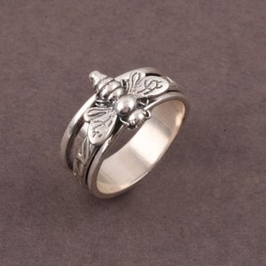 May include: A silver spinning ring featuring a bee design. The ring is made of metal and has a smooth finish.
