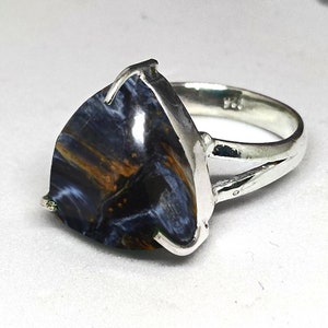 Puede incluir: Un anillo de plata con una piedra triangular de ojo de tigre azul y marrón.