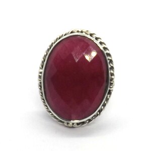 May include: A silver ring with a large, oval-shaped, faceted, dark red gemstone.
