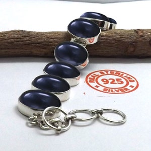 Op de afbeelding: Een sterling zilveren armband met een kettingsluiting en vijf ovale, donkerblauwe edelstenen. De armband heeft een stempel met de tekst "REAL STERLING 925 SILVER".