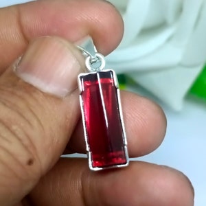 May include: A silver pendant with a rectangular red gemstone.