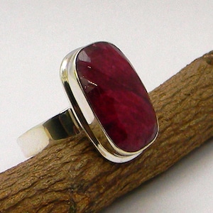May include: A silver ring featuring a large, rectangular, deep red gemstone.