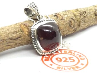 May include: A silver pendant with a dark red gemstone set in a square bezel. The pendant has a beaded border and is attached to a silver chain. The pendant is stamped with "925 Sterling Silver".