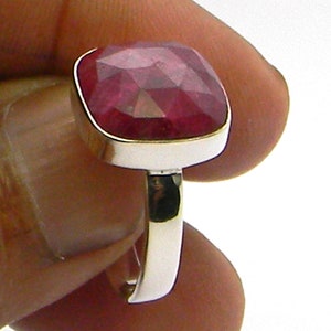 Pode incluir: Um anel de prata com uma grande pedra preciosa vermelha em forma de quadrado, um rubi.