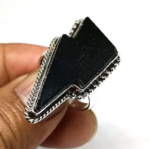 May include: A silver ring with a black lightning bolt shaped gemstone. The ring has a detailed silver band.