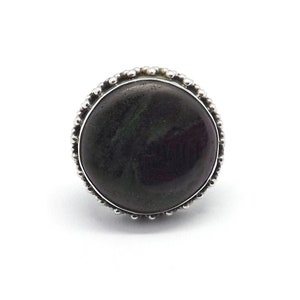 May include: A silver ring featuring a round, dark green and black gemstone set in a beaded bezel.