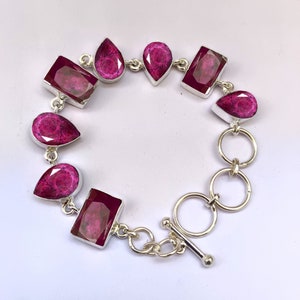 Peut inclure: Un bracelet en argent avec un fermoir à glissière présente un motif de pierres précieuses roses. Le bracelet présente une variété de formes de pierres précieuses roses, notamment rectangulaires et en forme de goutte.