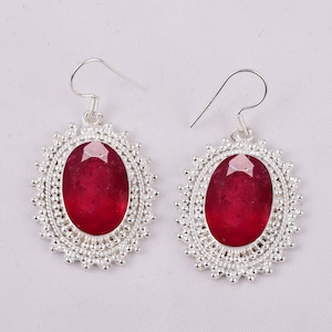 May include: A pair of silver earrings with a red gemstone set in a circular design.