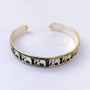 May include: A silver bangle bracelet with a repeating pattern of elephant silhouettes.