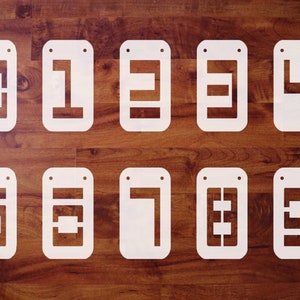 May include: Ten white wooden signs with different geometric shapes cut out of them. The signs are hanging on a wood background.