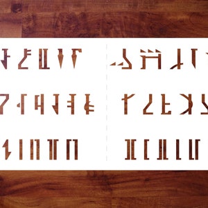 May include: White stencil sheet with a set of 26 letters and symbols in a stylized font. The letters are arranged in three rows, with the first row containing the letters A through G, the second row containing the letters H through N, and the third row containing the letters O through Z.