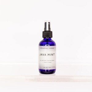 Könnte beinhalten: Eine blaue Glasflasche mit schwarzem Sprühkopf. Das Etikett lautet "Lavender Thorne Java Mint All Natural Coffee Room & Fabric Spray Net Wt. 4oz"