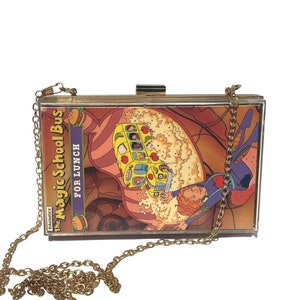 May include: A gold chain purse with a clear plastic front featuring a cartoon image of a yellow school bus with the text "The Magic School Bus FOR LUNCH" and a cartoon character.