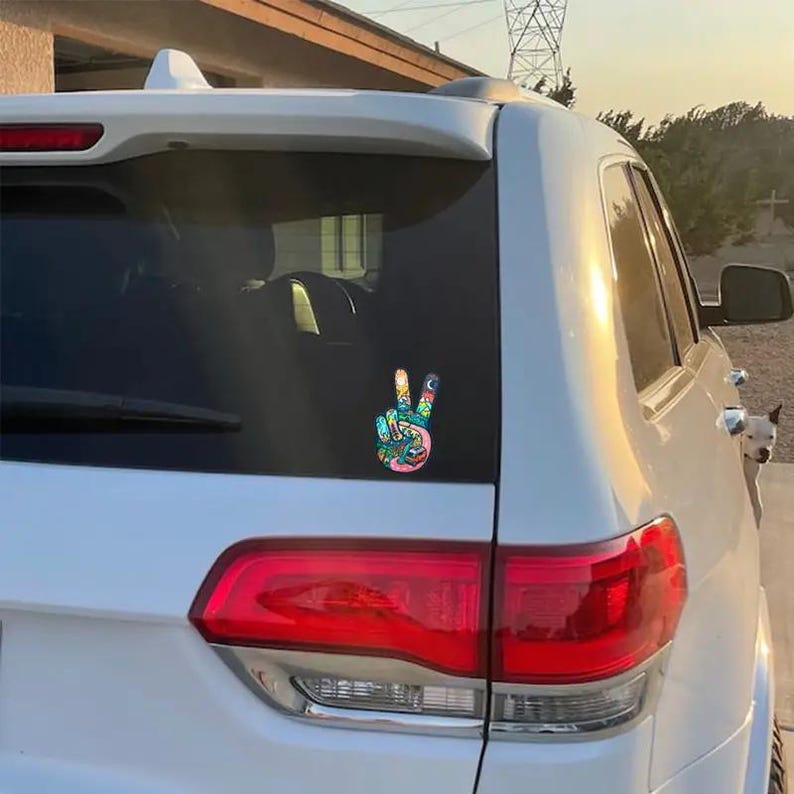 May include: A white SUV with a peace sign sticker on the back window. The sticker is colorful and features a peace sign with a variety of designs and patterns.