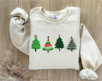 May include: A beige sweatshirt with a graphic of four stylized Christmas trees in green, red, and white with ornaments and a star on top.