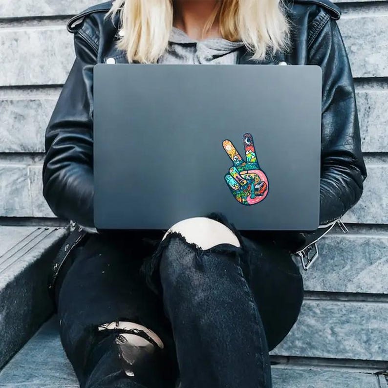 May include: A laptop computer with a colorful peace sign sticker on the lid. The sticker features a hand with a peace sign, filled with various nature-themed illustrations.