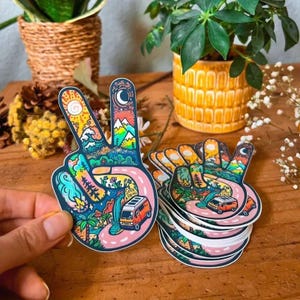 May include: A set of colorful peace sign stickers with a van, mountains, and other nature-inspired designs. The stickers are printed on white paper and have a glossy finish.