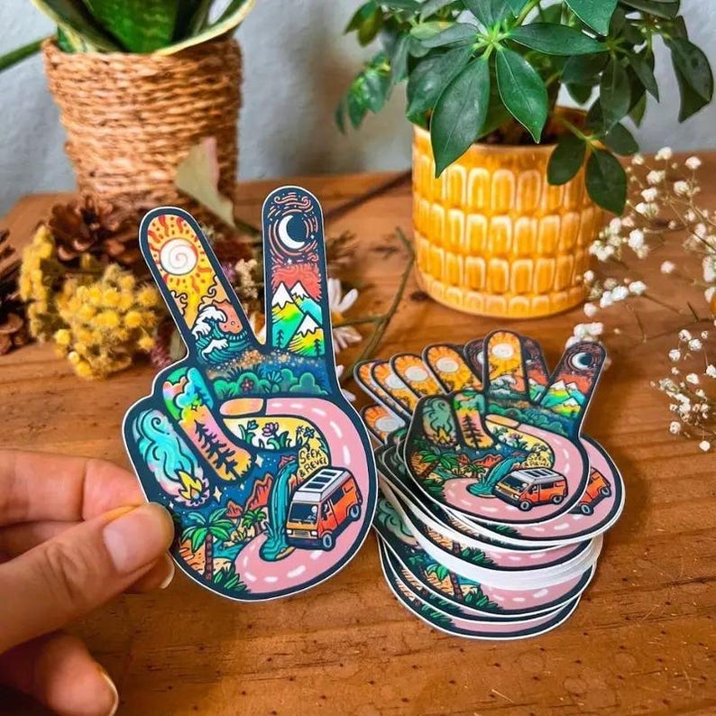 May include: A set of colorful peace sign stickers with a van, mountains, and other nature-inspired designs. The stickers are printed on white paper and have a glossy finish.