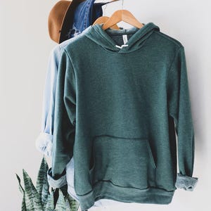 May include: A dark green hooded sweatshirt with a front pocket. The sweatshirt is hanging on a hanger.