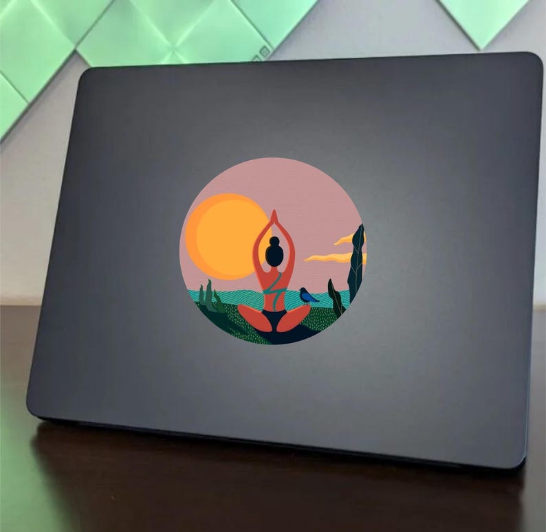 May include: A round sticker with a colorful illustration of a person in a yoga pose, a sunset, and a bird. The sticker is on a gray laptop.