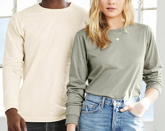 May include: Two people wearing long-sleeved shirts. The person on the left is wearing a cream-colored shirt and the person on the right is wearing a sage green shirt. Both people are wearing jeans.
