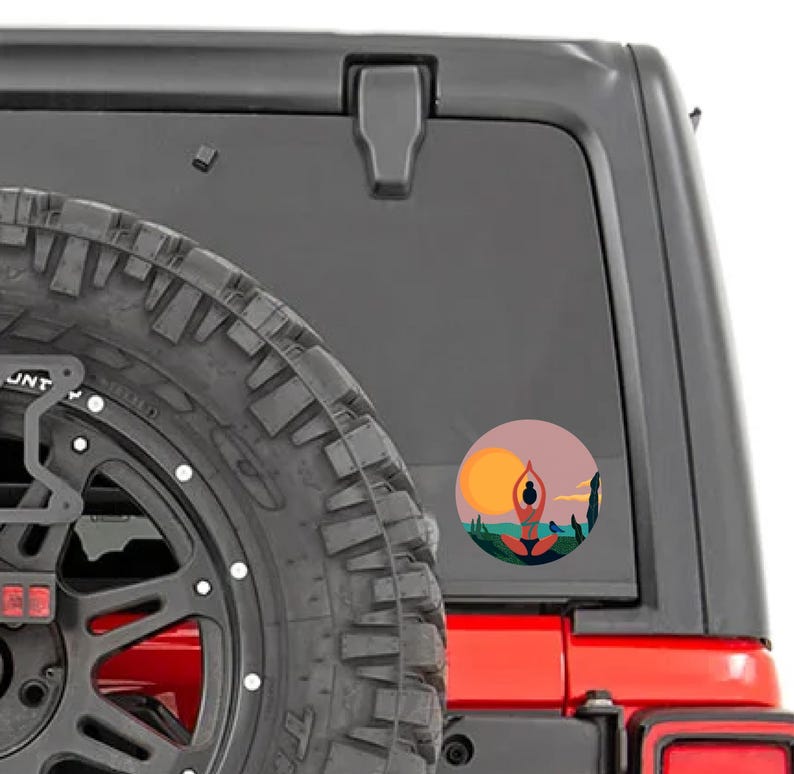 May include: A red Jeep with a black spare tire and a sticker on the back window. The sticker is a circle with a sunset scene and a person in a yoga pose.