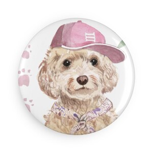 May include: A white and brown dog wearing a pink baseball cap with the number "III" on it. The dog is wearing a purple and brown bandana around its neck. The background is white with pink paw prints.