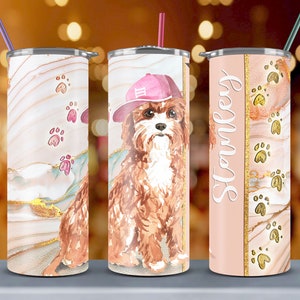 Puede incluir: Tres vasos de acero inoxidable con un diseño de mármol rosa y dorado. El vaso del centro presenta una ilustración de acuarela de un perro marrón con un sombrero rosa. El vaso de la derecha tiene el nombre "Stanley" escrito en él.