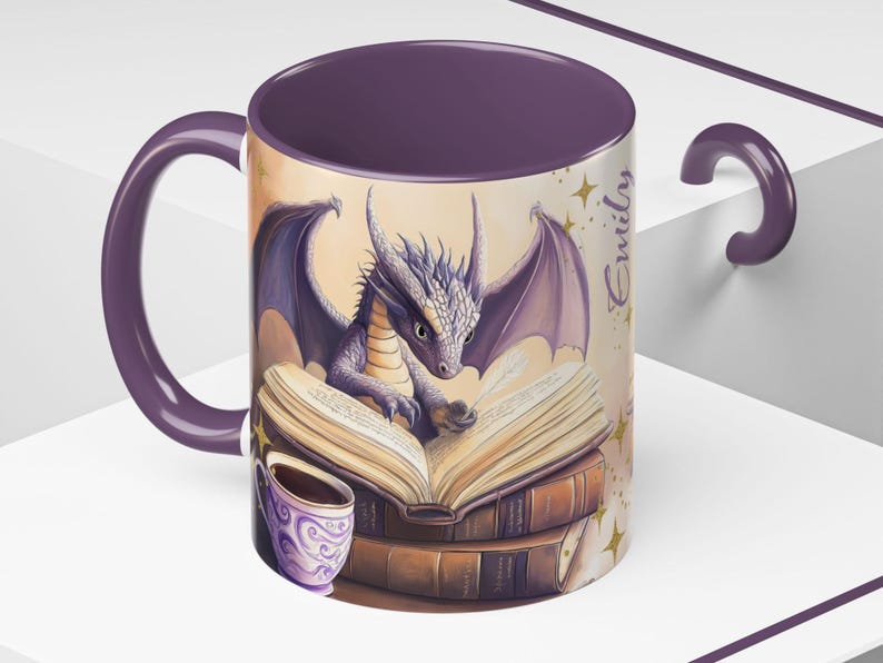Puede incluir: Taza de cer&aacute;mica morada con un drag&oacute;n leyendo un libro y una taza de caf&eacute;. La taza tiene el nombre "Emily" escrito en el lateral.