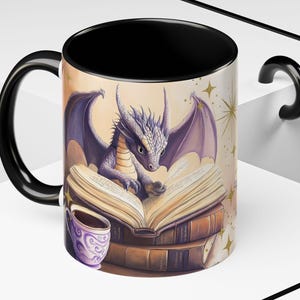 Puede incluir: Una taza de caf&eacute; negra con un drag&oacute;n morado leyendo un libro. El drag&oacute;n est&aacute; sentado sobre una pila de libros. La taza tiene un asa negra y un interior blanco. El fondo es amarillo claro con estrellas doradas.
