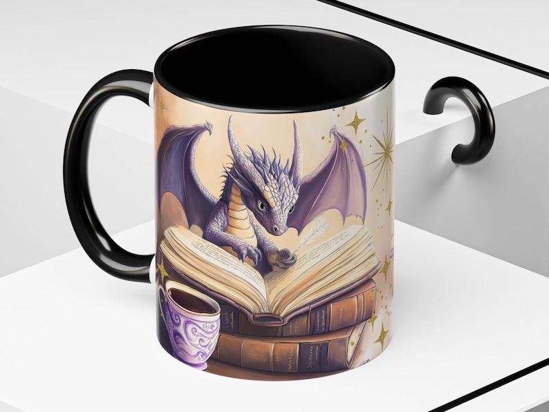 Puede incluir: Una taza de caf&eacute; negra con un drag&oacute;n morado leyendo un libro. El drag&oacute;n est&aacute; sentado sobre una pila de libros. La taza tiene un asa negra y un interior blanco. El fondo es amarillo claro con estrellas doradas.