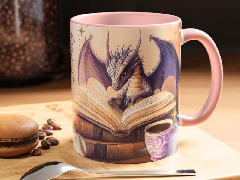 Puede incluir: Una taza de cer&aacute;mica rosa con un drag&oacute;n leyendo un libro. El drag&oacute;n es morado y tiene alas. El libro est&aacute; abierto y tiene una pluma en la parte superior. La taza est&aacute; rodeada de una pila de libros.