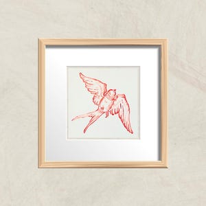 May include: A framed print of a red line drawing of a swallow in flight. The swallow is depicted with its wings spread wide and its tail feathers trailing behind it.