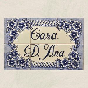 Pode incluir: Um sinal de azulejos azuis e brancos com as palavras "Casa D. Ana" em escrita cursiva.