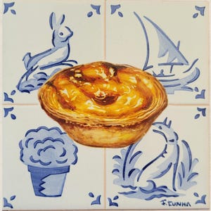 Pode incluir: Azulejo quadrado com uma pintura detalhada de uma torta de creme dourada. O azulejo é rodeado por elementos decorativos azuis e brancos, incluindo um coelho, um veleiro e motivos florais. Assinatura do artista visível.