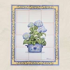 Pode incluir: Painel de azulejos decorativo com um design floral azul e branco. A imagem central mostra uma hortênsia em vaso com flores azuis e folhas verdes. O azulejo é emoldurado com uma borda amarela e azul.